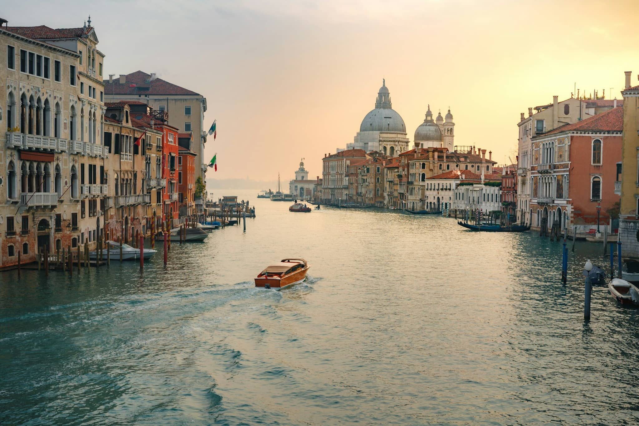 A working boat on a Venice canal at sunset, residential facades on the opposite bank.